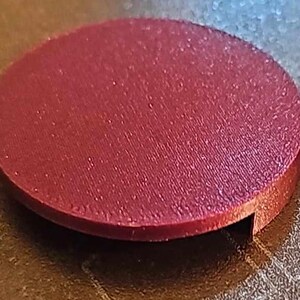 May include: A round, maroon-colored plastic disc with a slightly raised edge and a small notch cut out of the side.
