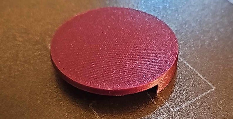 May include: A round, maroon-colored plastic disc with a slightly raised edge and a small notch cut out of the side.
