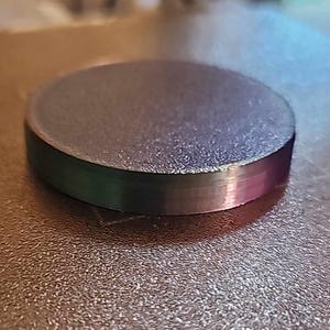 May include: A round, dark gray, plastic disc with a textured surface.