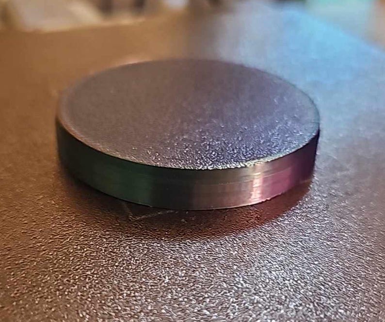 May include: A round, dark gray, plastic disc with a textured surface.