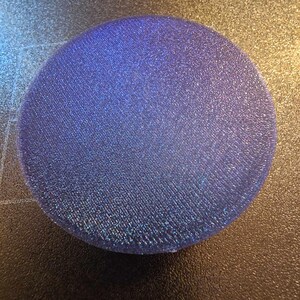 May include: A round, iridescent blue glitter coaster. The coaster is made of a textured material and has a slightly raised edge.