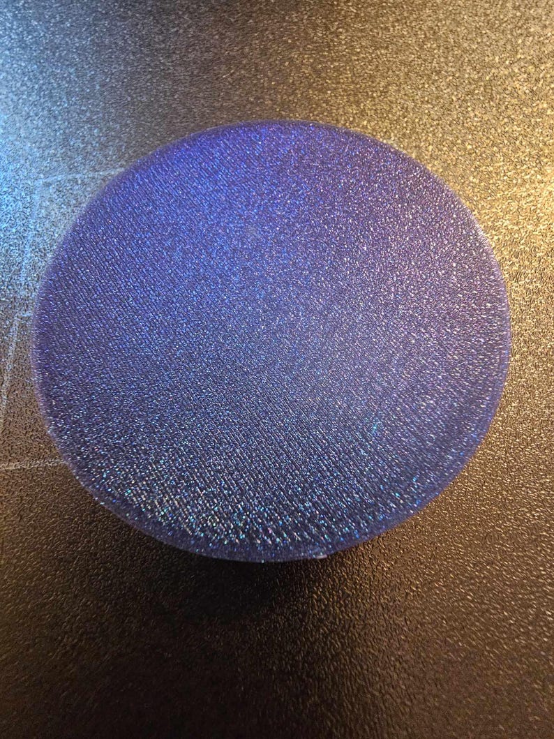 May include: A round, iridescent blue glitter coaster. The coaster is made of a textured material and has a slightly raised edge.