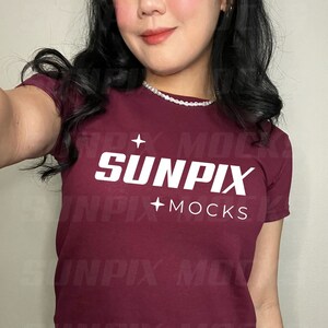 Può includere: T-shirt bordeaux con la scritta bianca "SUNPIX MOCKS". La maglietta a maniche corte sembra essere realizzata in un materiale morbido. La modella indossa jeans blu.