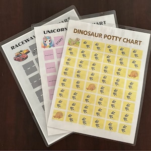 May include: Three laminated potty training charts with colorful illustrations. The first chart features a race car, the second chart features a unicorn, and the third chart features a dinosaur with the text "Dinosaur Potty Chart".