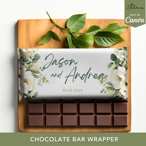 Könnte beinhalten: Eine Schokoladentafel mit einer individuellen Verpackung mit den Namen "Jason und Andrea" und dem Datum 06.03.2024, mit floralen Akzenten. Die Tafel liegt auf einem Holzbrett mit grünen Blättern.