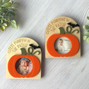 May include: Two wooden photo frames shaped like pumpkins. Each frame features an orange pumpkin cutout with the text "Cutest Pumpkin in the Patch!" and a small bat silhouette. The frames hold baby photos.