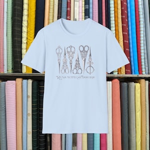 Puede incluir: Camiseta azul claro con un gráfico de cinco tijeras vintage y el texto "Runs with Scissors".