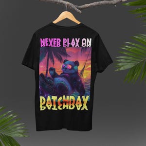 Peut inclure: T-shirt noir avec un graphique d'un panda portant un casque et des lunettes de soleil se relaxant dans un hamac sur une plage au coucher du soleil. Le texte "NEVER PLAY ON PATCHDAY" est imprimé sous le graphique.