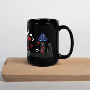 Puede incluir: Taza de café de cerámica negra con un diseño gráfico blanco y rojo que presenta una figura encapuchada, código y el texto "404>" impreso en la parte delantera.
