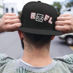 Puede incluir: Una gorra de béisbol negra y roja con la palabra "ROFL" en letras blancas y una cara sonriente en el medio de la palabra.