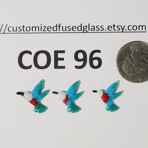 May include: Three miniature glass hummingbird figurines with turquoise wings, white and red bodies, and black beaks. The text "COE 96" is above the hummingbirds. A coin is next to the figurines.