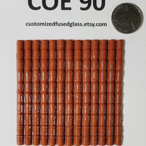 May include: A collection of small, rectangular, terracotta-colored glass tiles arranged in a grid pattern. The tiles are next to a US quarter coin for size comparison. The text "COE 90" and a website address are visible at the top.