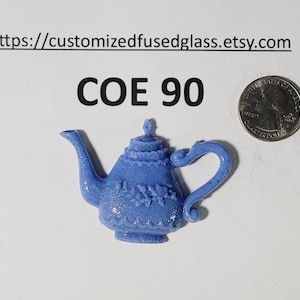 May include: A small, light blue decorative teapot with floral detailing. The teapot is made of fused glass and is next to a US quarter coin. The text "COE 90" is above the teapot. The Etsy shop URL is at the top.