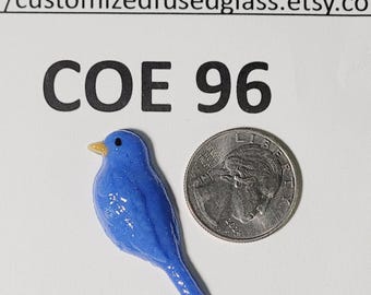 May include: A small blue glass bird figurine with a yellow beak and a black eye, positioned next to a United States quarter coin for scale. The text COE 96 and customizedfusedglass.etsy.com are printed above the bird.