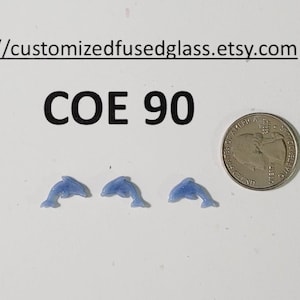 May include: Three small, blue dolphin-shaped glass pieces next to a quarter coin. The text "COE 90" is above the dolphins. The Etsy shop URL is at the top of the image.