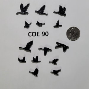May include: A white background with black silhouette cutouts of geese flying in different directions. The text "COE 90" is printed in black on the white background. A US quarter is included for scale.