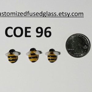 May include: Three miniature fused glass bee figurines with black and yellow stripes and white wings. The text "COE 96" is above the bees. A quarter coin is next to the bees for size comparison. The Etsy shop name is at the top.