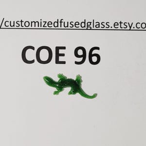 May include: A small, dark green glass lizard figurine. The text "COE 96" is printed above the lizard. The Etsy shop URL is printed at the top of the image.