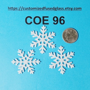 May include: Three white snowflake-shaped glass pieces labeled COE 96, positioned next to a United States quarter coin for scale. The text https://customizedfusedglass.etsy.com is printed at the top of the bright blue background.