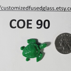 May include: A small, glossy, bright green fused glass turtle figurine positioned next to a silver United States quarter coin for scale. The text COE 90 and the URL customizedfusedglass.etsy.com are printed in black above the turtle.