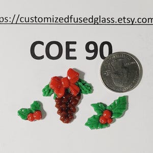 May include: Three fused glass holiday decorations including a pinecone with a red bow and two holly berry clusters with green leaves. The text reads https://customizedfusedglass.etsy.com and COE 90. A US quarter coin is shown for scale.
