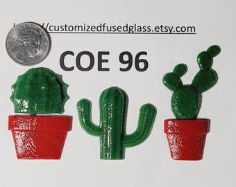 May include: Three green glass cactus shapes, two in red pots and one without, displayed with a US quarter coin for scale. The text "COE 96" and "customizedfusedglass.etsy.com" is visible above the items on a plain white background.