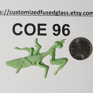 May include: A light green fused glass praying mantis figurine positioned next to a United States quarter coin for scale. The text COE 96 and the URL https://customizedfusedglass.etsy.com are printed in black above the glass insect figure.