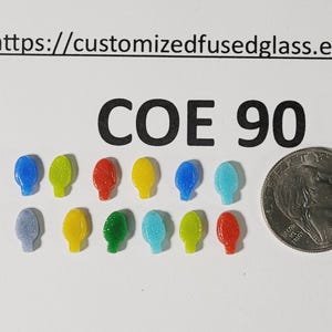 May include: Twelve small, colorful, translucent glass light bulb shapes arranged in two rows. The text 'COE 90' and a URL are printed above. A US quarter coin is placed to the right for scale, showing the small size of the glass pieces.