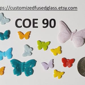 May include: A collection of colorful glass butterfly shapes in various sizes and hues, including blue, orange, green, yellow, red, and lavender. The text "COE 90" is displayed. A quarter coin is included for size reference. The Etsy shop URL is visible.