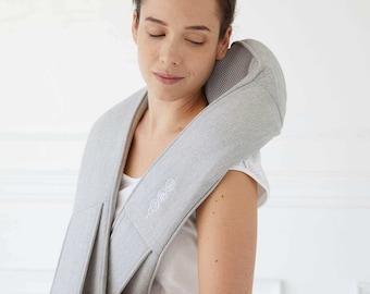 May include: A gray neck and shoulder massager with a mesh panel and a white logo. The massager is worn by a person with their eyes closed.