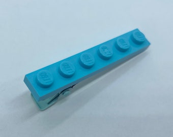 May include: A light blue hair clip shaped like a row of five LEGO bricks. Each brick has the word "LEGO" embossed on it.