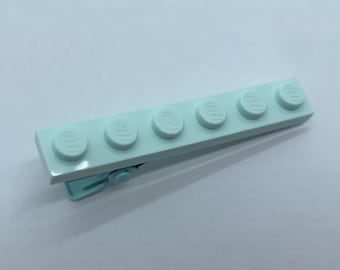 May include: A light blue hair clip with six small, light blue Lego bricks attached to it.