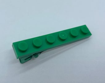 May include: A green plastic hair clip with five Lego bricks attached to it.