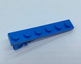 May include: A blue Lego brick with five studs, a clip on the bottom, and a smooth surface.