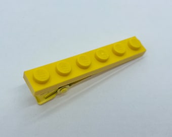 May include: A yellow plastic hair clip shaped like a row of five Lego bricks.