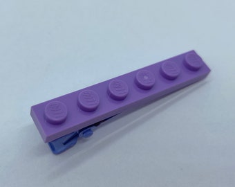 May include: A purple plastic hair clip made from five connected Lego bricks. Each brick has the word "LEGO" printed on it.