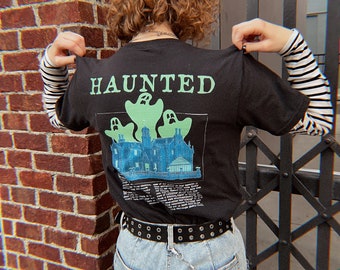 May include: Black t-shirt with a graphic print of a haunted house and ghosts. The text "HAUNTED" is printed on the shirt.
