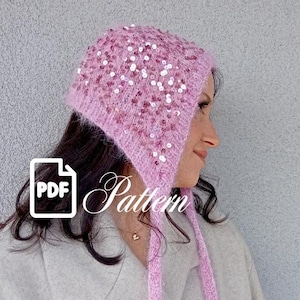May include: A light pink knitted hat with sequins. The hat has ear flaps and ties. The word "Pattern" is written in cursive on the hat. A PDF icon is in the lower left corner.