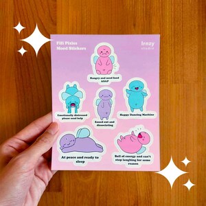 May include: A sheet of Fifi Pixies mood stickers featuring cartoon characters in various emotional states. The stickers include phrases like "Hangry and need food ASAP" and "Happy Dancing Machine." The Irnzy studio logo is visible.