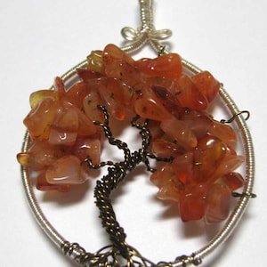May include: A silver wire tree of life pendant with a brown wire trunk and branches. The tree is decorated with carnelian stones in shades of orange and red.
