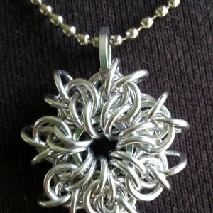 May include: A silver chain necklace with a silver metal pendant in the shape of a flower. The pendant is made of many small, interconnected rings.