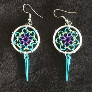 May include: A pair of silver earrings with a turquoise and purple mandala design and a turquoise spike hanging from the bottom.