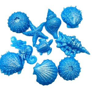 May include: A collection of blue sea creature figurines, including a starfish, seahorse, turtle, and various seashells. The figurines have a shimmering, glittery finish and are arranged on a white background.