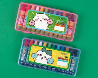 Op de afbeelding: Twee kleurpotloodsets in doorzichtige plastic cases, één roze en één blauwe, op een groene achtergrond. Elke case bevat 12 kleurpotloden en een label met een cartoonfiguur. De roze case heeft een witte beer, en de blauwe een witte beer met een strik.