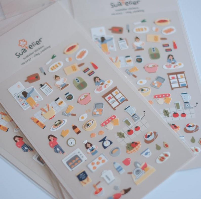 May include: Sheets of decorative stickers featuring cooking-themed illustrations. The stickers include images of kitchen tools, food items, and people cooking. The color palette includes soft pastels and earth tones, with a focus on a cooking theme.
