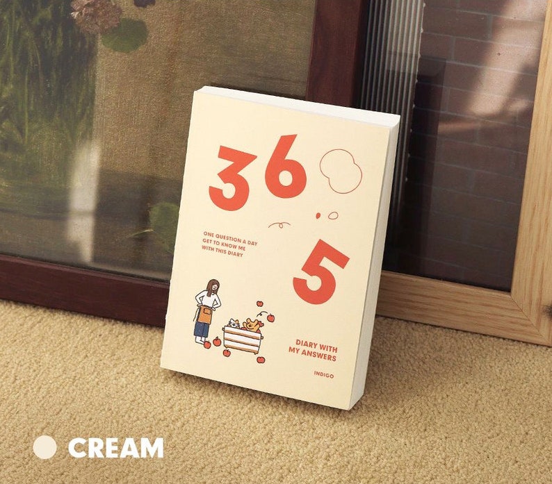 May include: A cream-colored journal with the text "365 Diary with My Answers" and "One Question a Day Get to Know Me with This Diary". The cover features a cartoon illustration of a person with a basket of apples and the numbers 365 and 5 in red.