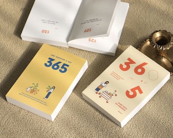 May include: A yellow journal with the text "One Question a Day 365" in blue. The journal has a white spine and a white cover. The journal is on a brown surface.