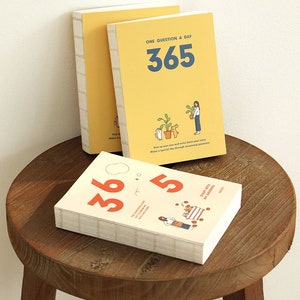 May include: Two yellow and white journals with the text "One Question a Day 365" and illustrations of a person and a cat with plants. The bottom journal has the text "365 Daily Notes of Myself".