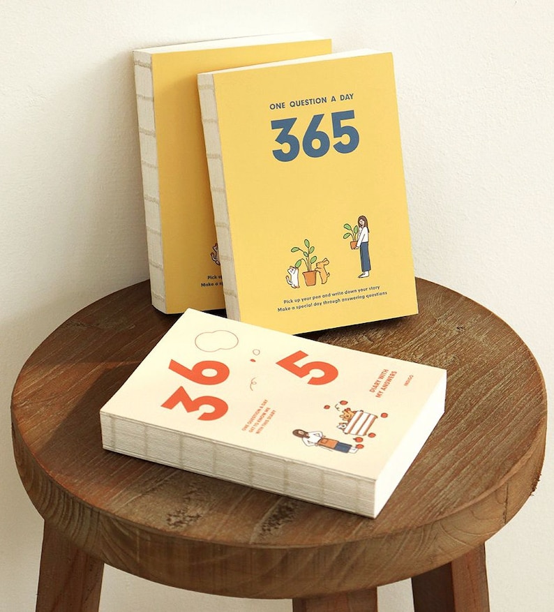 May include: Two yellow and white journals with the text "One Question a Day 365" and illustrations of a person and a cat with plants. The bottom journal has the text "365 Daily Notes of Myself".