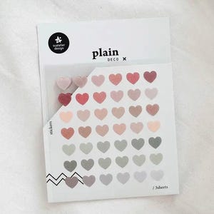 Może przedstawiać: Opakowanie naklejek w kształcie serca w różnych odcieniach różu, czerwieni i szarości. Opakowanie jest oznaczone napisem "plain DECO" i zawiera tekst "stickers" oraz "/3sheets". Naklejki ułożone są w rzędach i kolumnach.